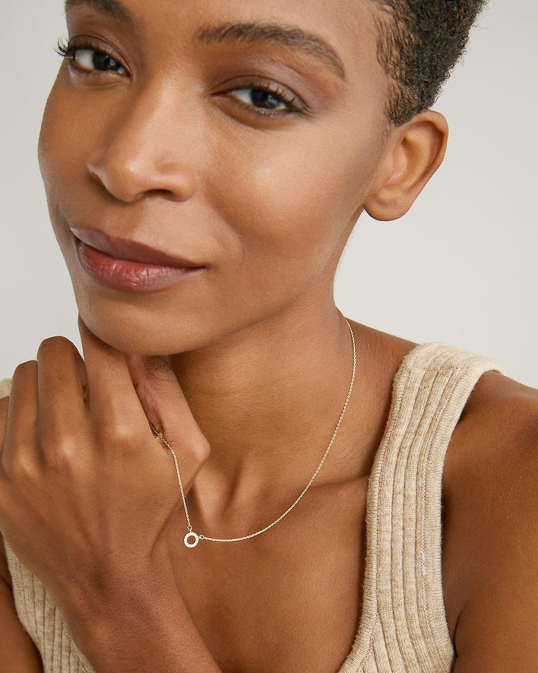 Model wearing delicate gold circle pendant necklace against neutral background