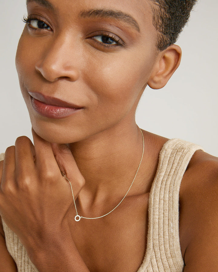 Model wearing delicate gold circle pendant necklace against neutral background