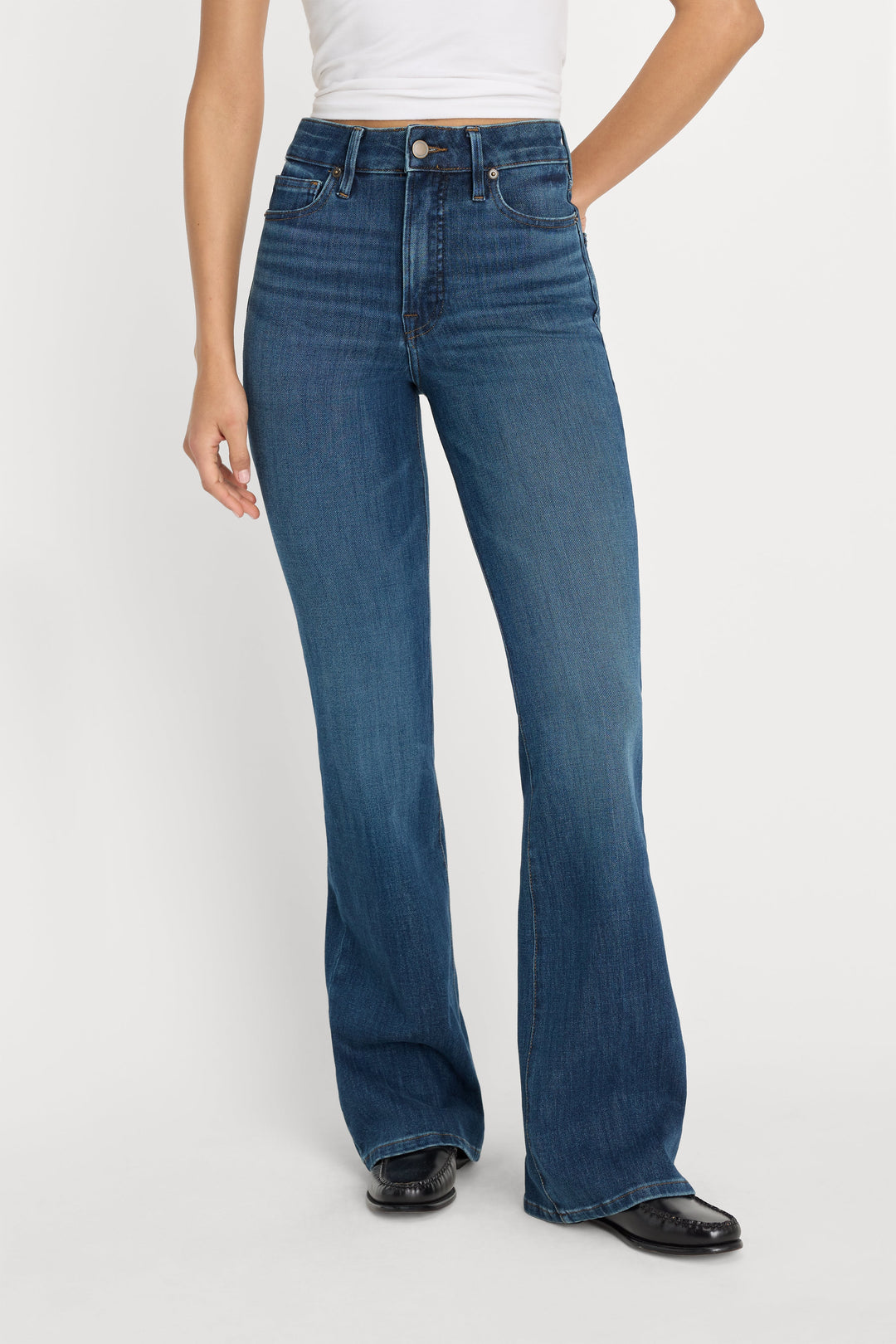 Woman wearing high-waisted blue bootcut jeans with white top and black shoes