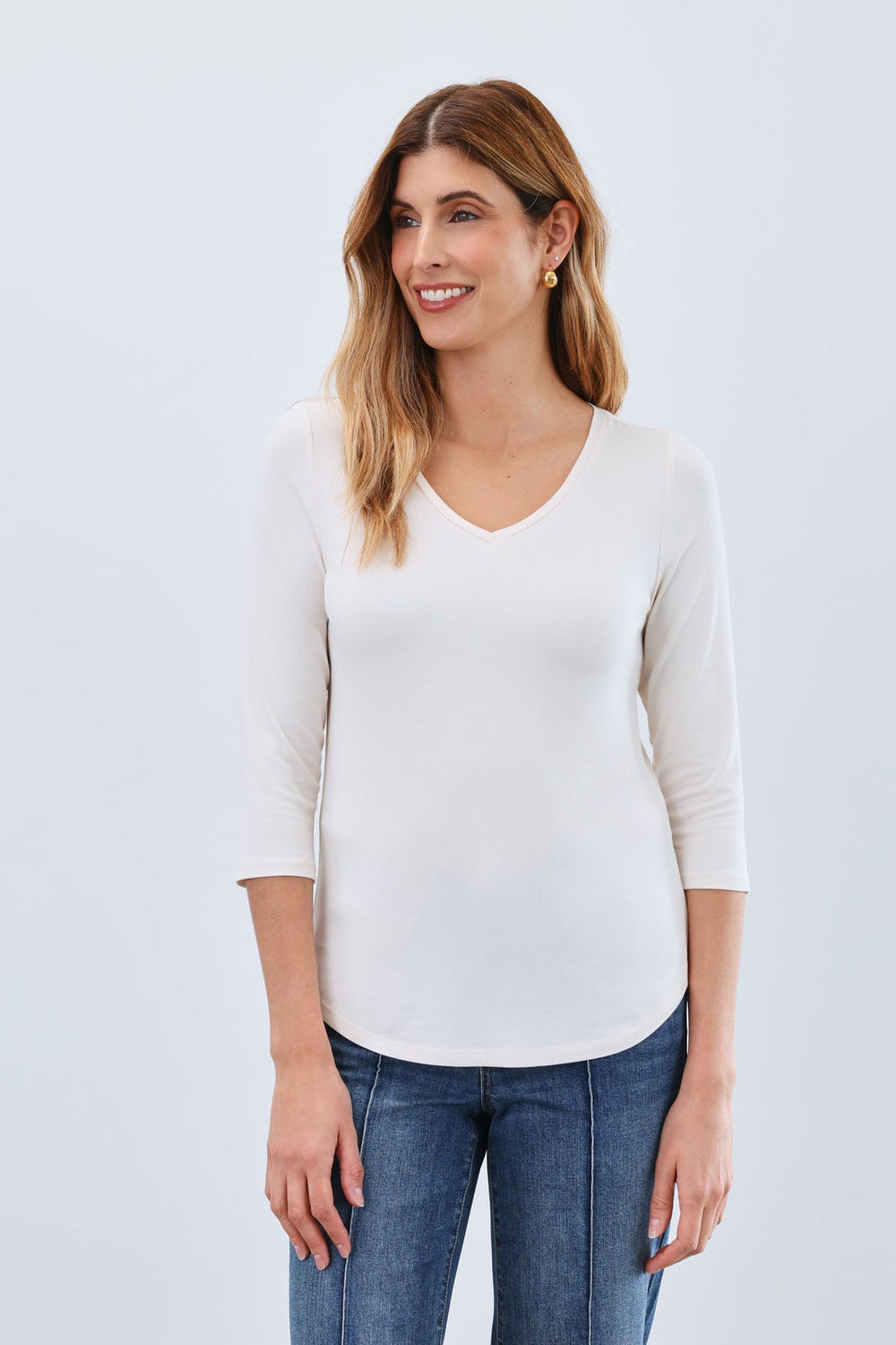 Woman wearing a cream 3/4 sleeve V-neck fitted top with blue jeans
