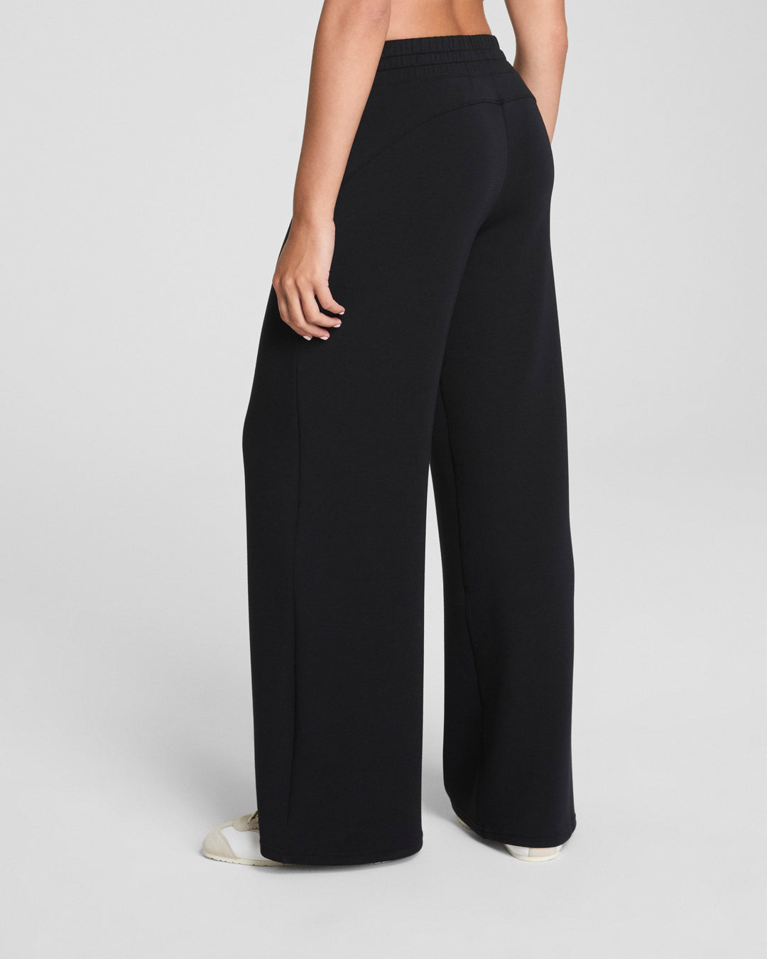 Model wearing black wide leg pants from behind on white background
