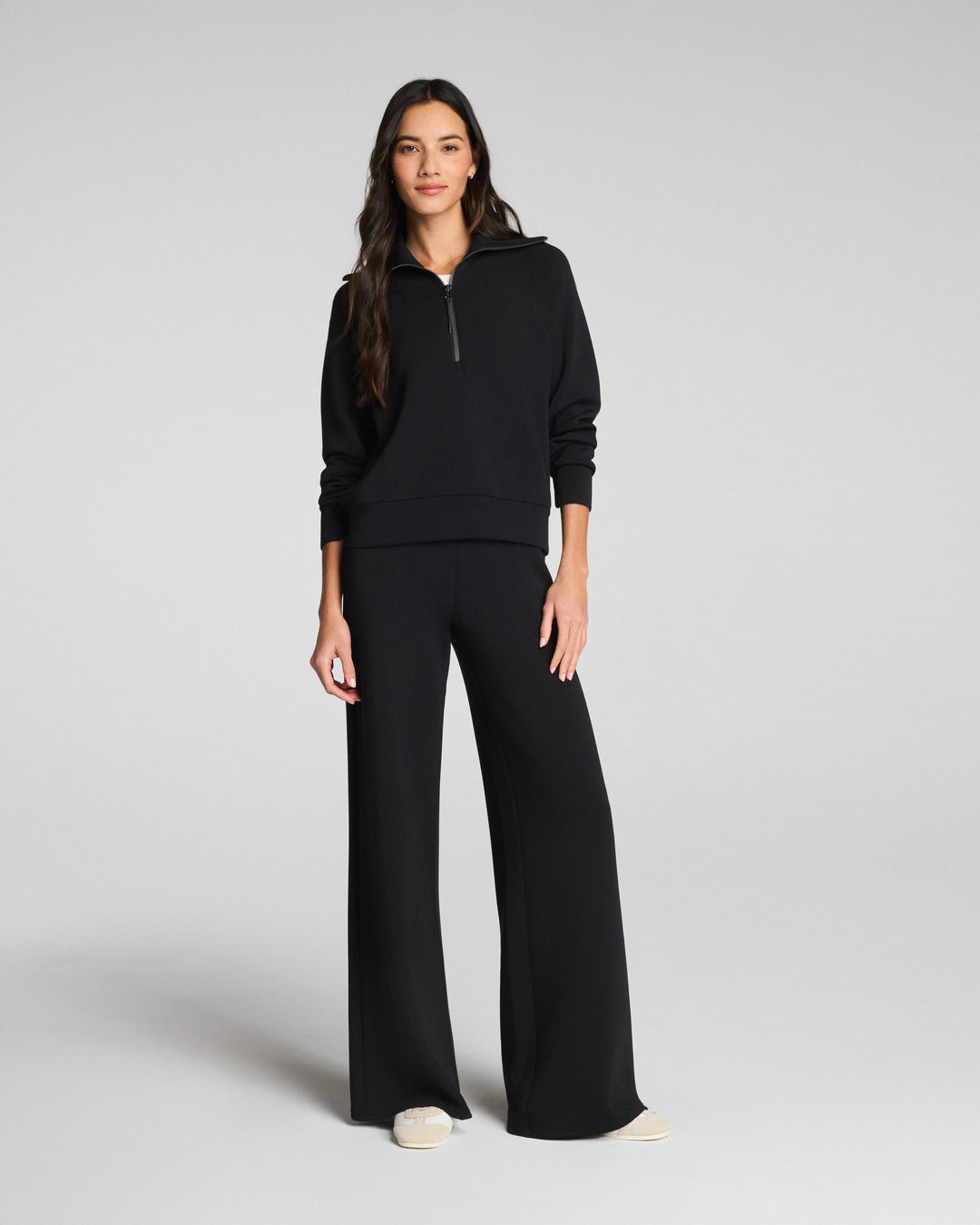 Woman wearing black wide leg pants and matching hoodie in studio photo