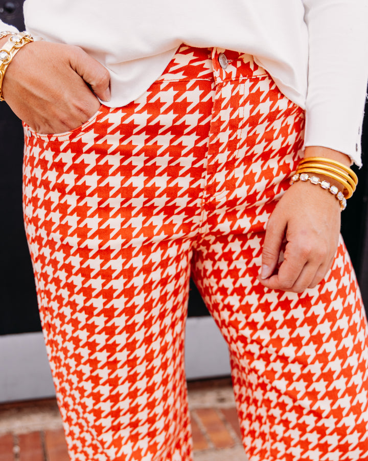 A close-up of a person wearing bright orange and white houndstooth pants, styled with a white top and gold bracelets.
