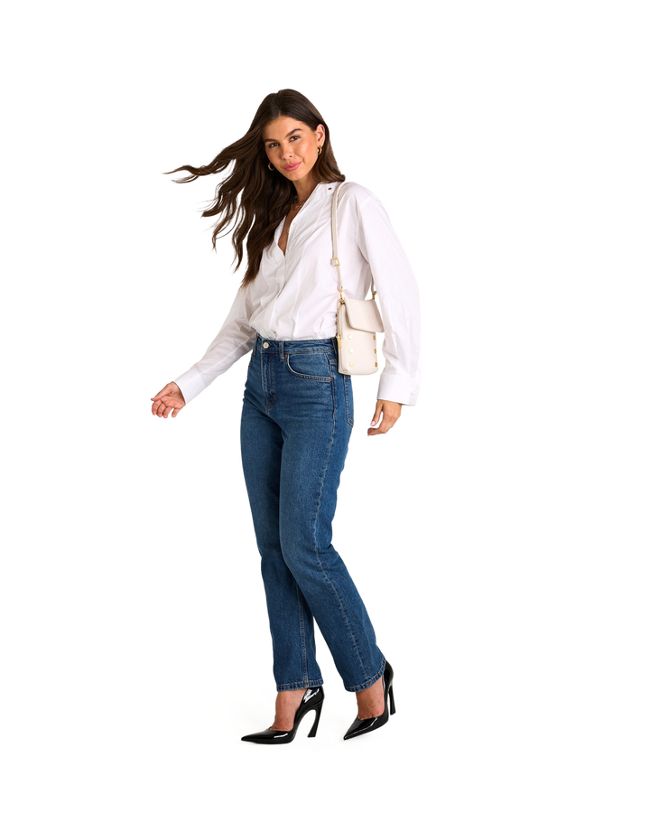 Model wearing white blouse and jeans carrying Hammitt VIP Mobile crossbody bag in calla lily white with brushed gold hardware
