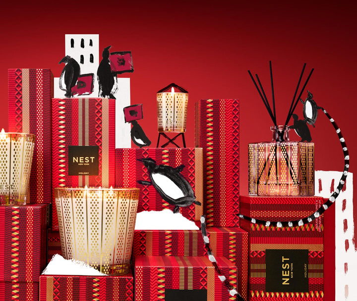 NEST New York Holiday 3-wick candle in gold glass vessel with festive red and gold boxes