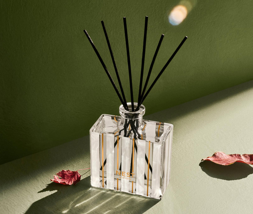 NEST New York reed diffuser in clear glass bottle with black reeds and autumn leaves