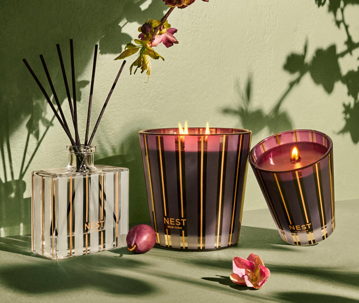 NEST New York Autumn Plum reed diffuser with striped gold black candles on green surface