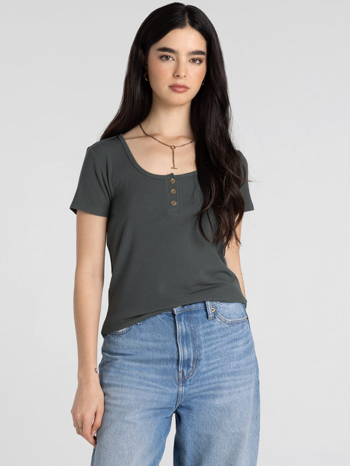 Woman wearing dark olive ribbed henley short-sleeve top with blue jeans