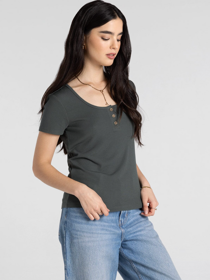Woman wearing olive green ribbed henley short-sleeve top with buttons and blue jeans