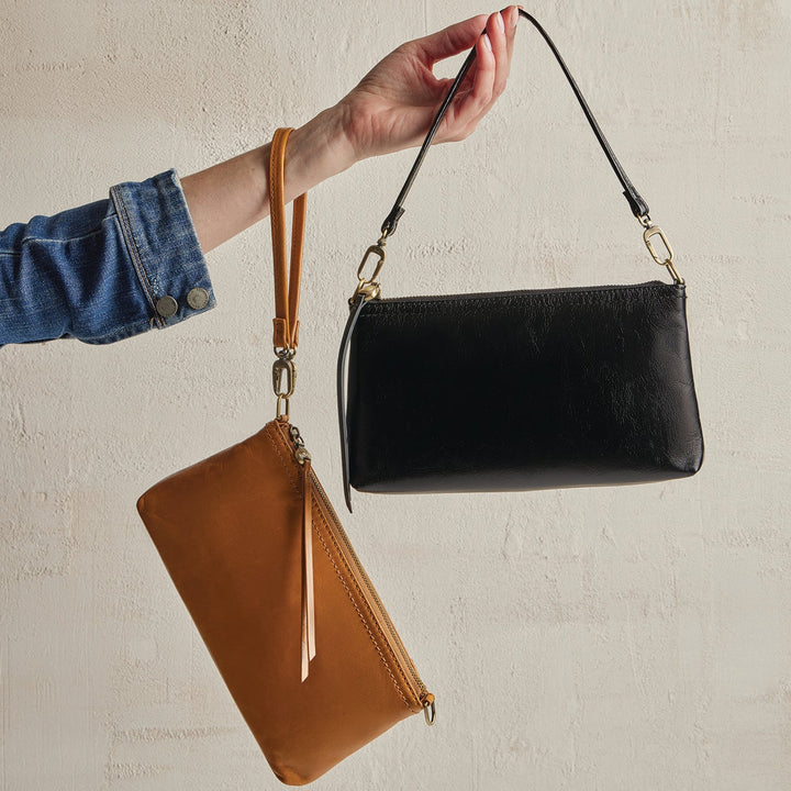 Hand holding black leather crossbody bag with detachable cognac brown wristlet pouch