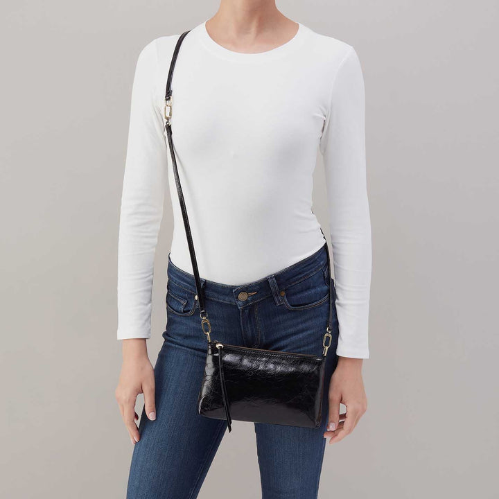 Black leather crossbody bag worn across body with white top and jeans