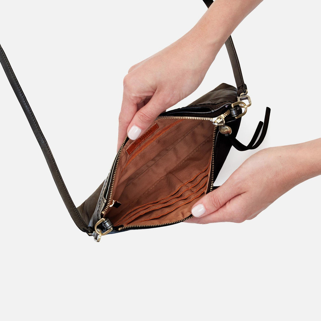 Hands opening black leather crossbody bag showing brown interior with card slots