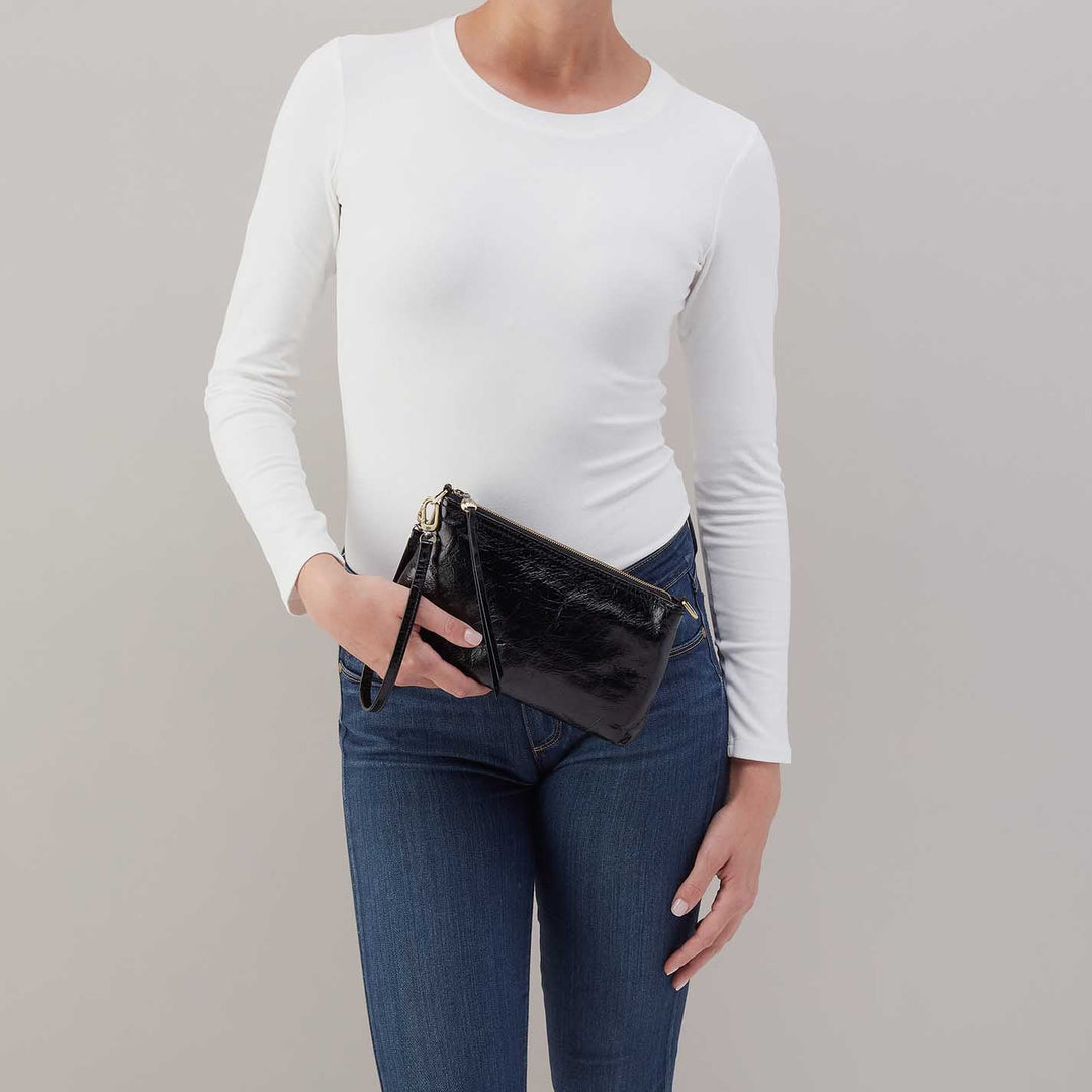 Woman holding black leather clutch purse with wrist strap, wearing white top and jeans