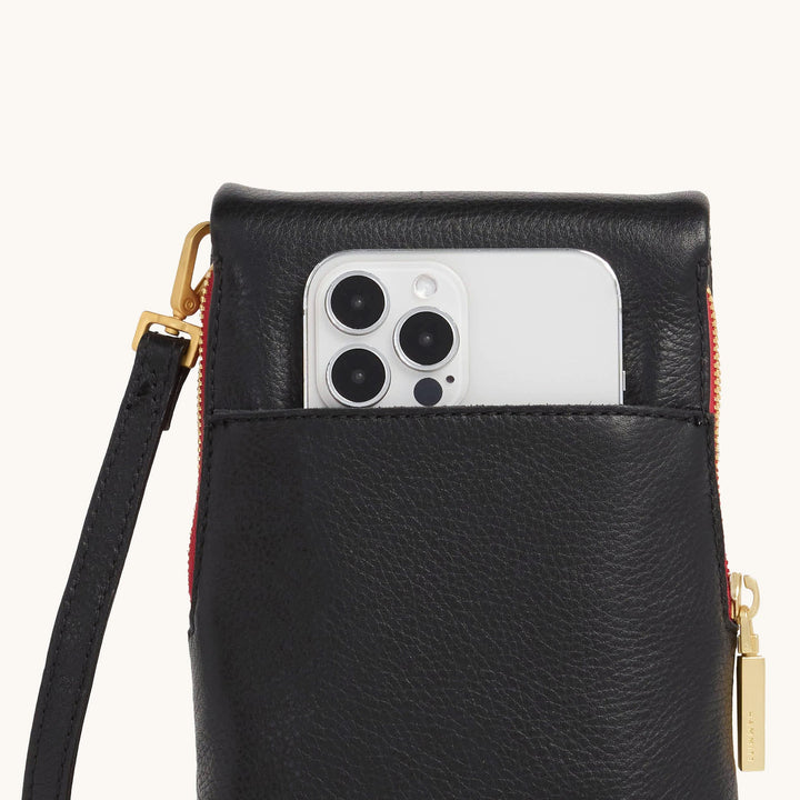 Hammitt VIP Mobile black leather crossbody bag with red zip and gold hardware holding iPhone